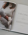 Open book showing a person wearing knitted mittens and a sweater with the word 'Villing' on a light background.