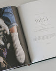 Open book with a page titled 'PIELI' featuring a person wearing white socks and blue jeans.