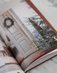 Open book with a photograph of a door and Christmas decorations on a marble surface