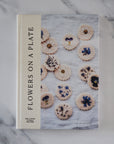 Book titled 'Flowers on a Plate' with floral cookies on a marble background