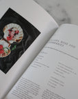Open book with a recipe for scallops, rose, and blackberries on a marble surface.