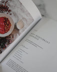 Open book with a recipe for Rosy Redcurrant Porridge on a marble surface.