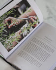 Open book with a photo of hands pruning herbs and text on a marble surface