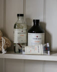Bath products including bottles and a bar of soap on a shelf against a white paneled wall.