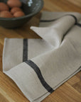 Beige towel with black trim on a wooden surface with eggs in the background