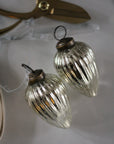 Two clear glass ornaments with bronze bases on a white surface with scissors in the background.