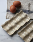Two brown eggs on a textured ceramic dish with a striped cloth in the background.