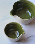 Two green ceramic pitchers on a marble surface