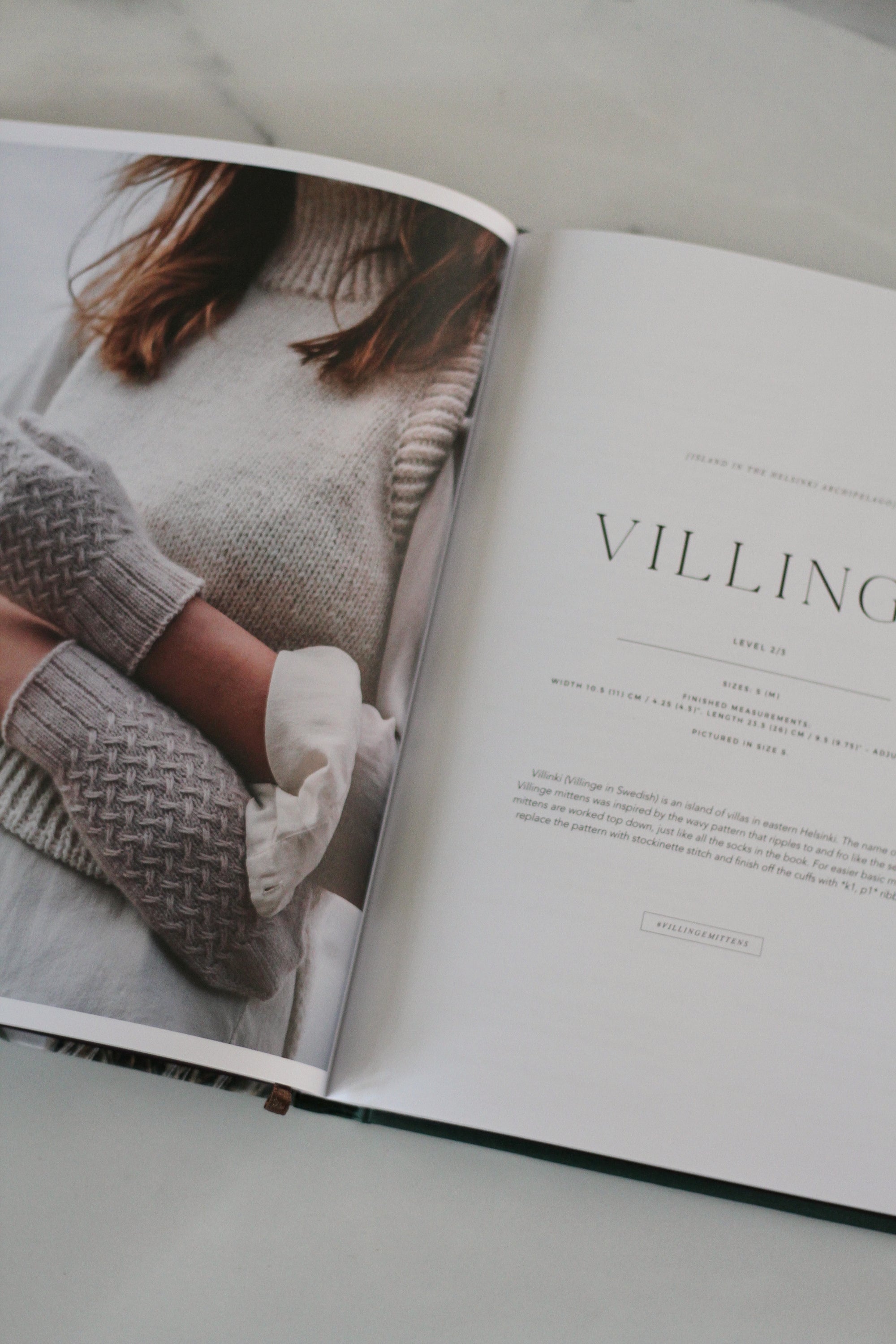 Open book showing a person wearing knitted mittens and a sweater with the word 'Villing' on a light background.