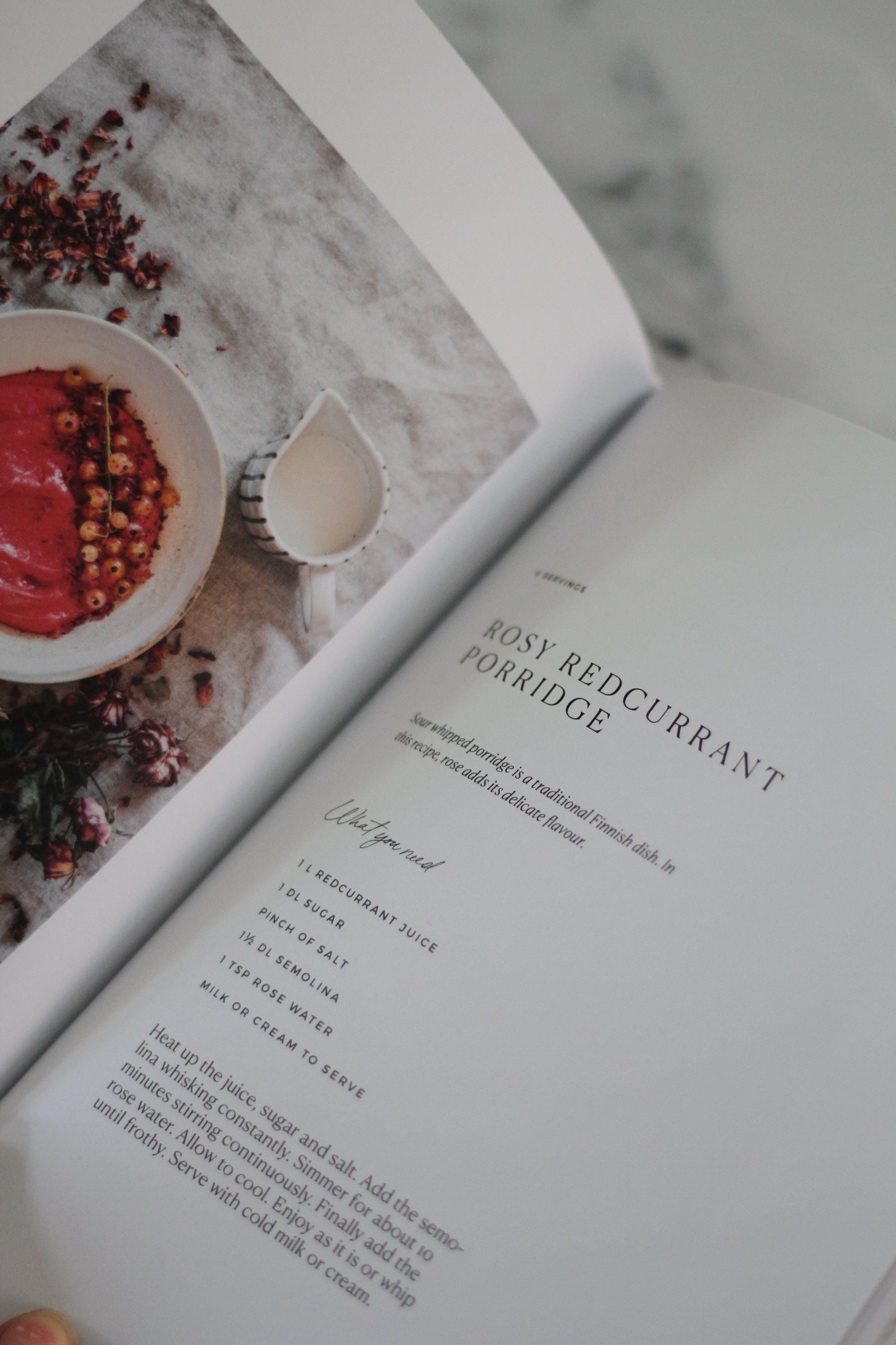 Open book with a recipe for Rosy Redcurrant Porridge on a marble surface.