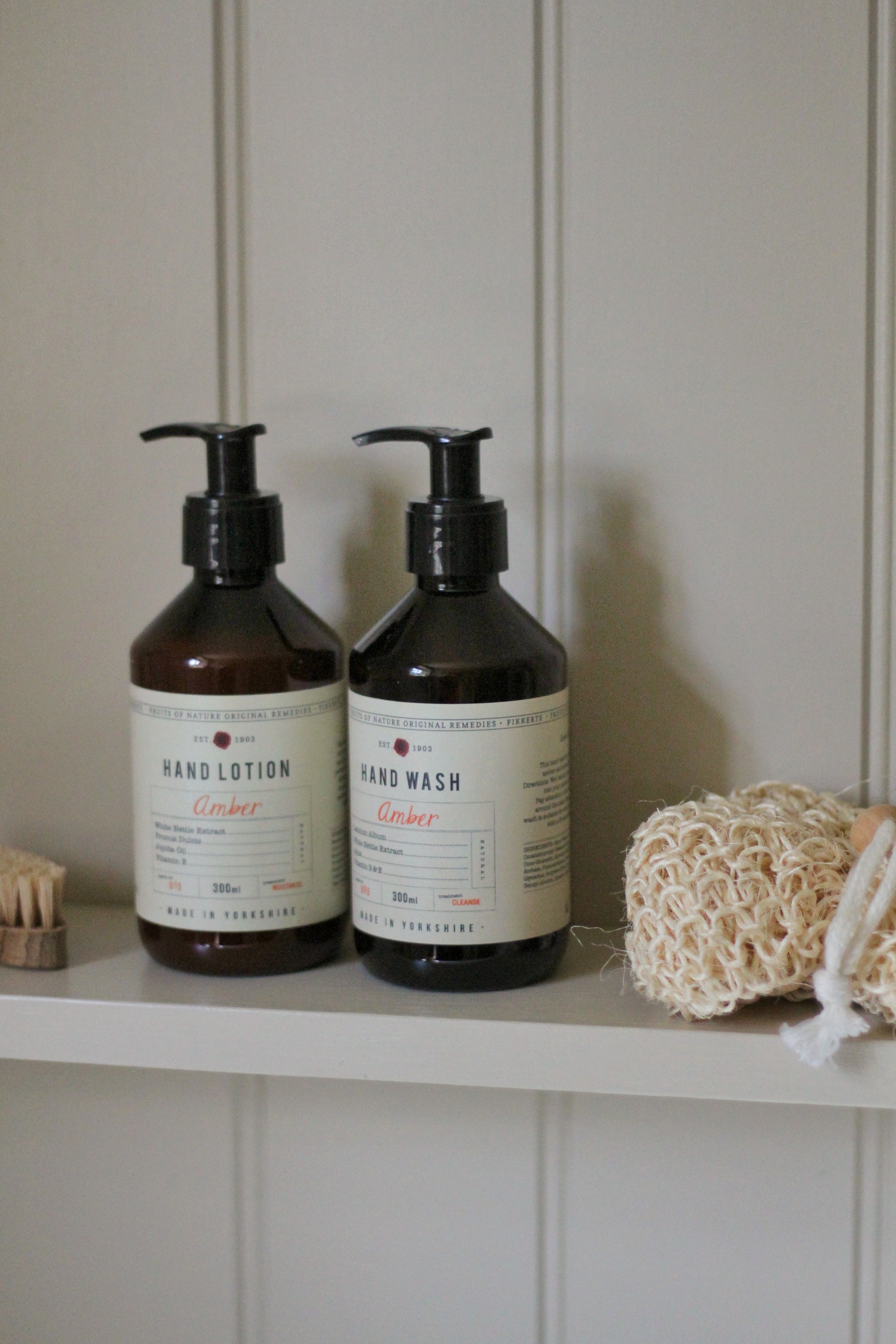 Two bottles of hand lotion and hand wash on a shelf with a loofah and brush.