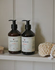 Two bottles of hand lotion and hand wash on a shelf with a loofah and brush.
