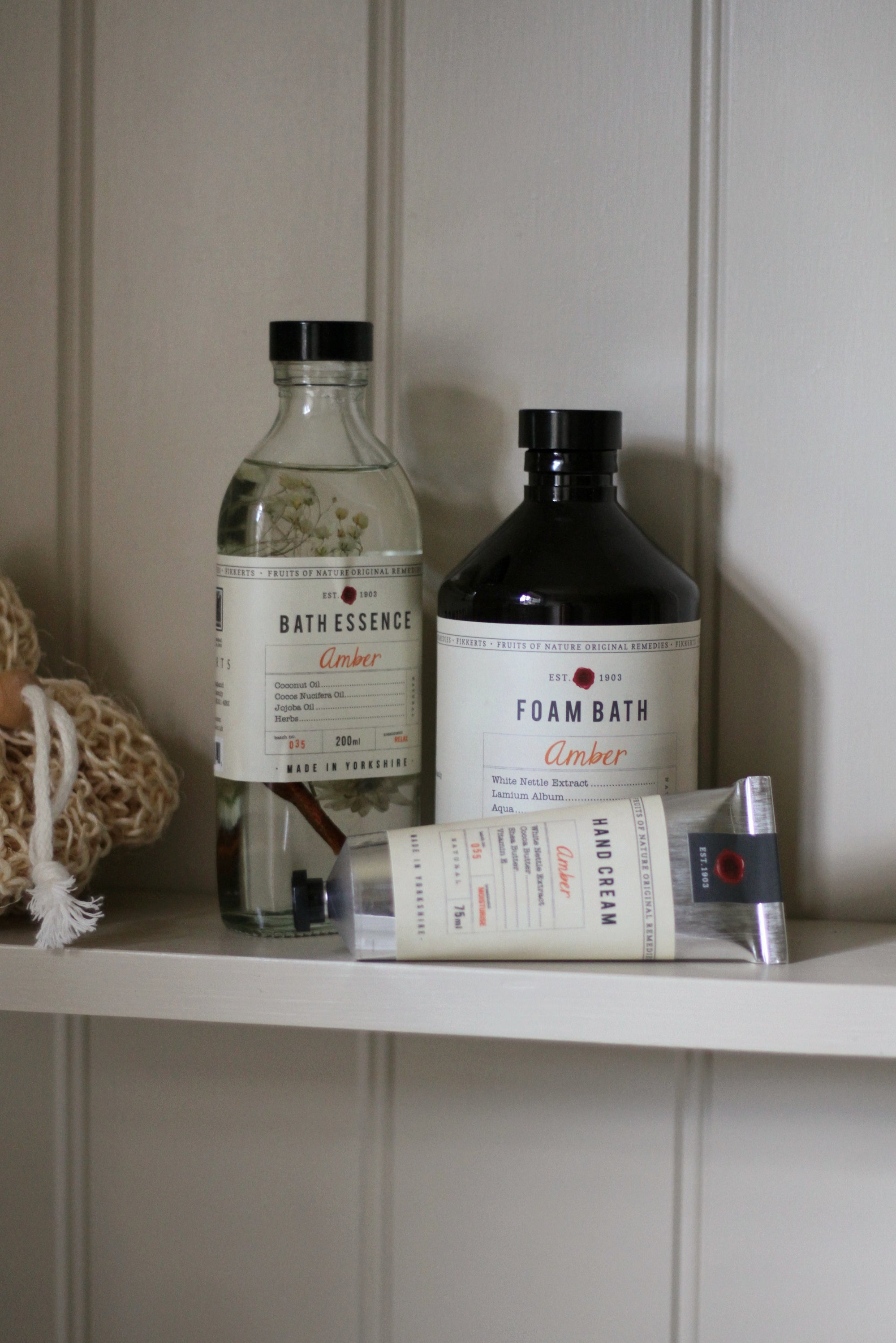 Bath products including bottles and a bar of soap on a shelf against a white paneled wall.