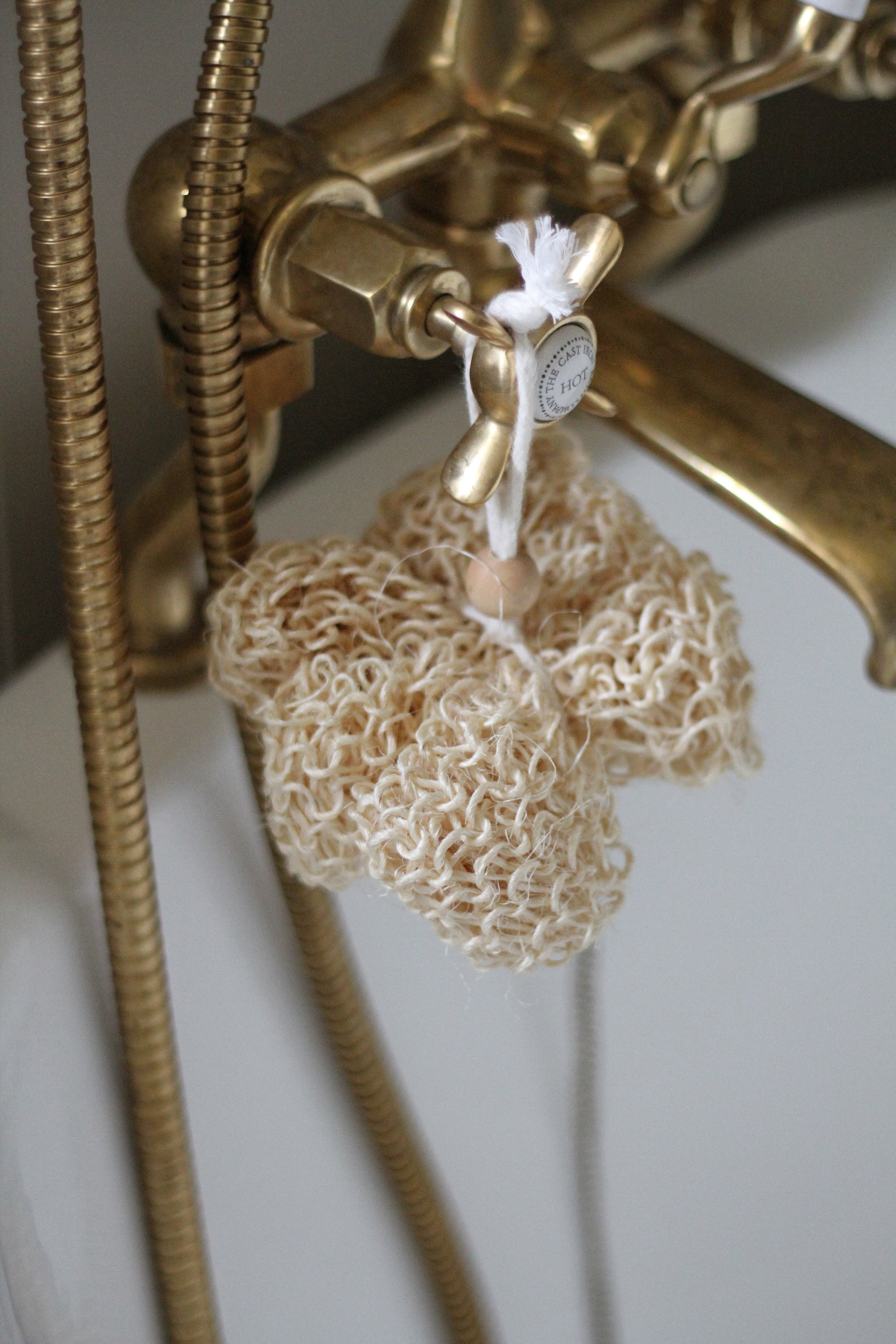 Brass shower head with a loofah hanging from it against a white background