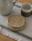 Stack of woven coasters on a striped fabric surface with ceramic items.