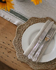 Set table with white plate, silver knife, and fork on a woven placemat with sunflowers in the background.
