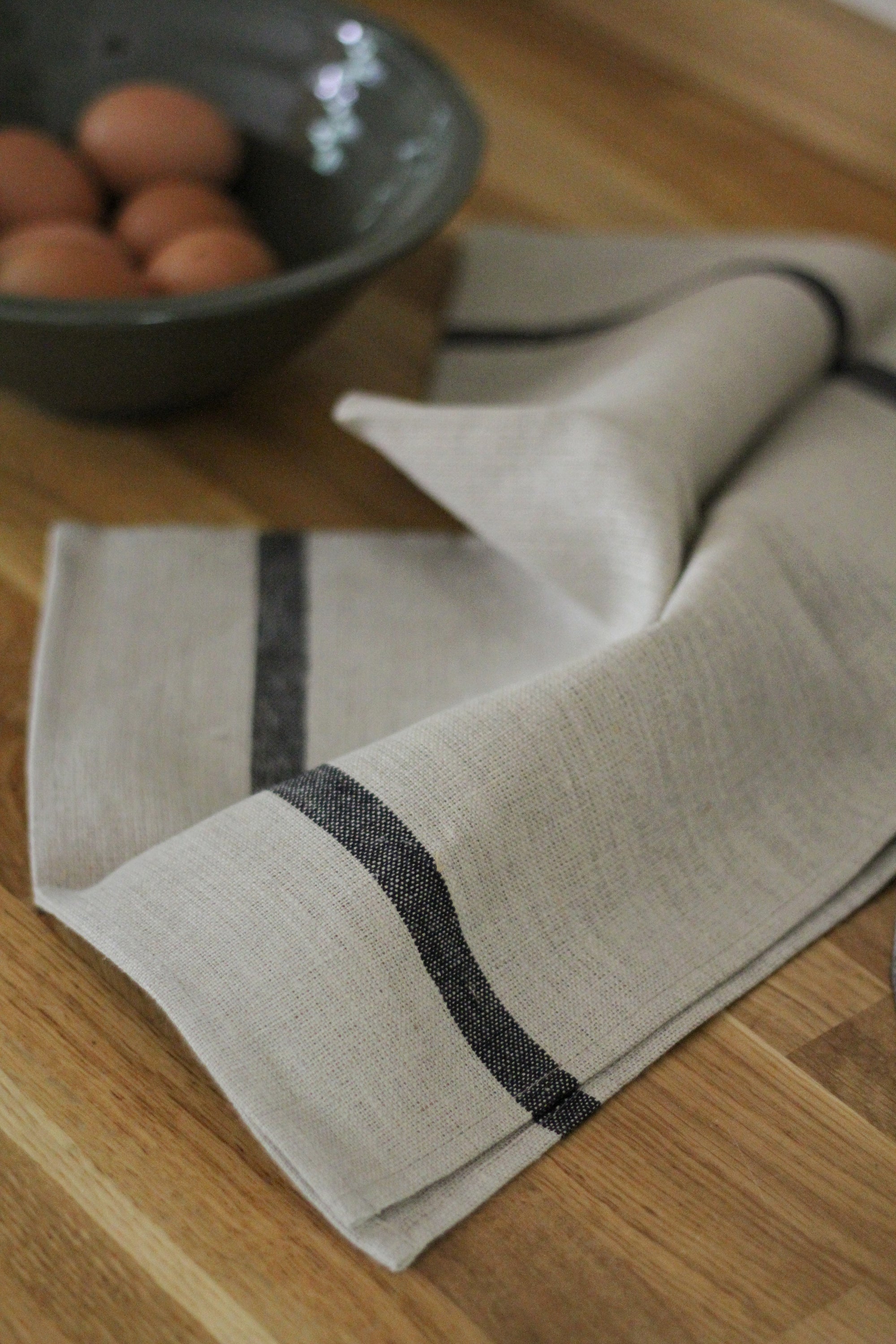 Beige towel with black trim on a wooden surface with eggs in the background
