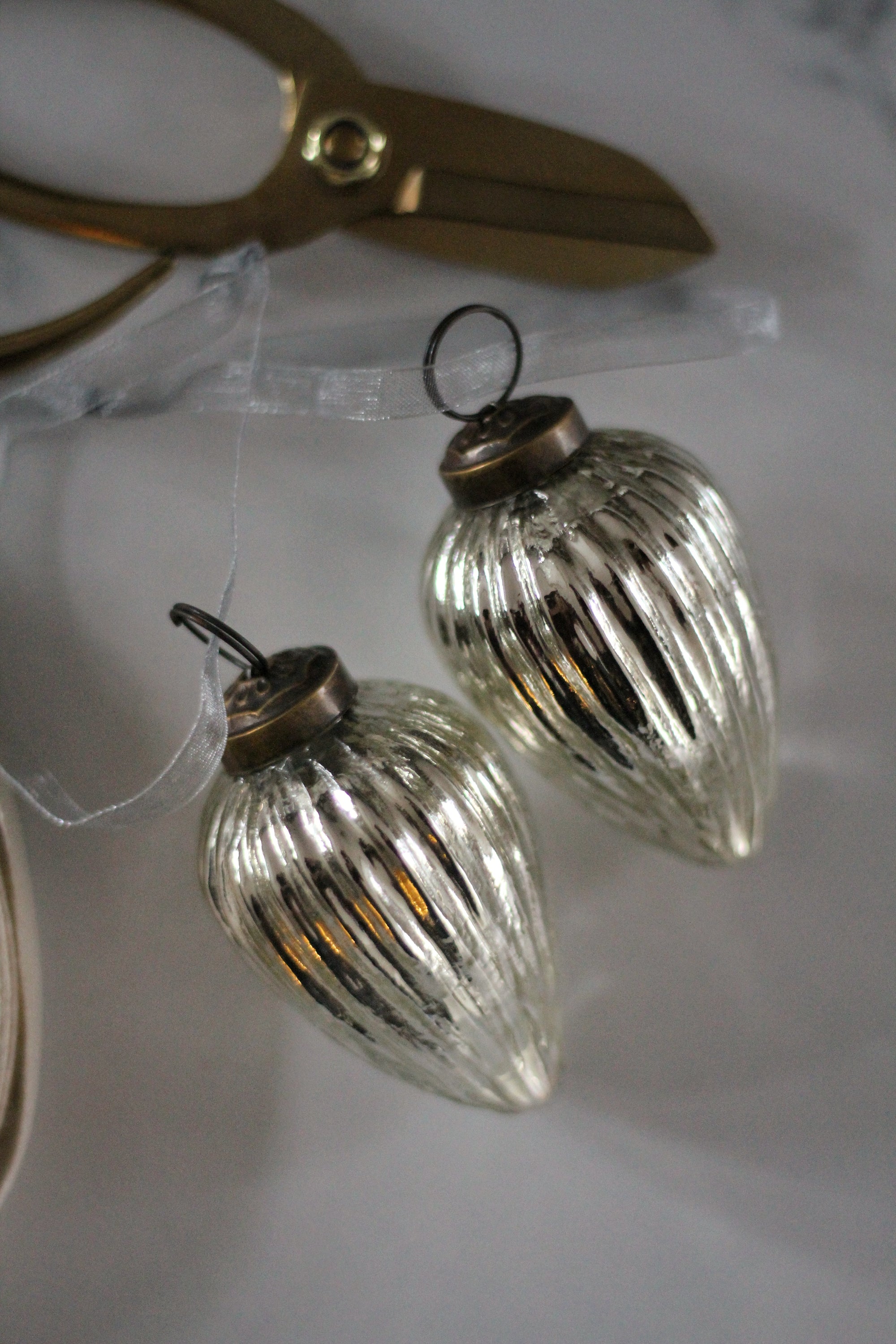 Two clear glass ornaments with bronze bases on a white surface with scissors in the background.