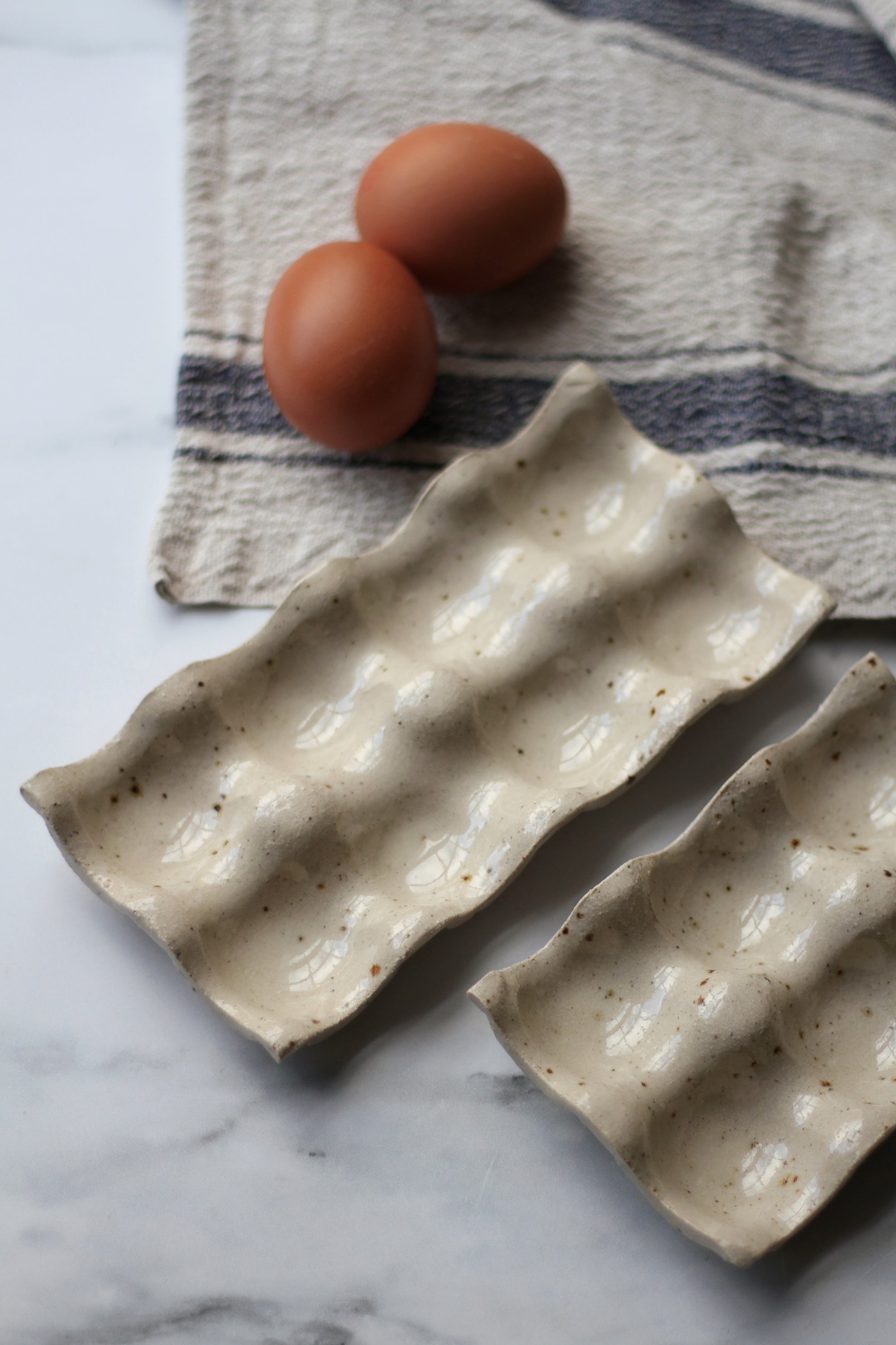 Two brown eggs on a textured ceramic dish with a striped cloth in the background.