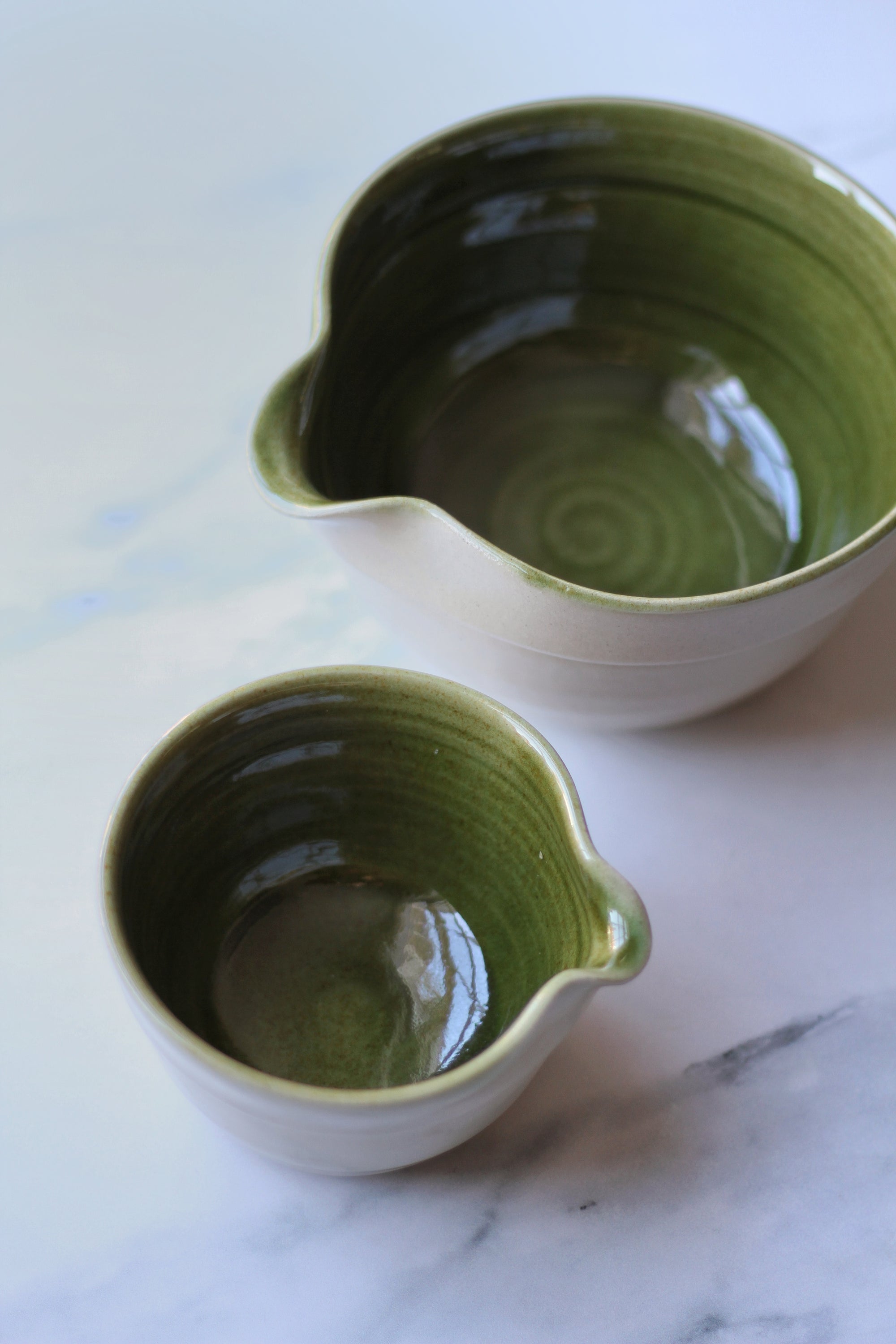 Two green ceramic pitchers on a marble surface