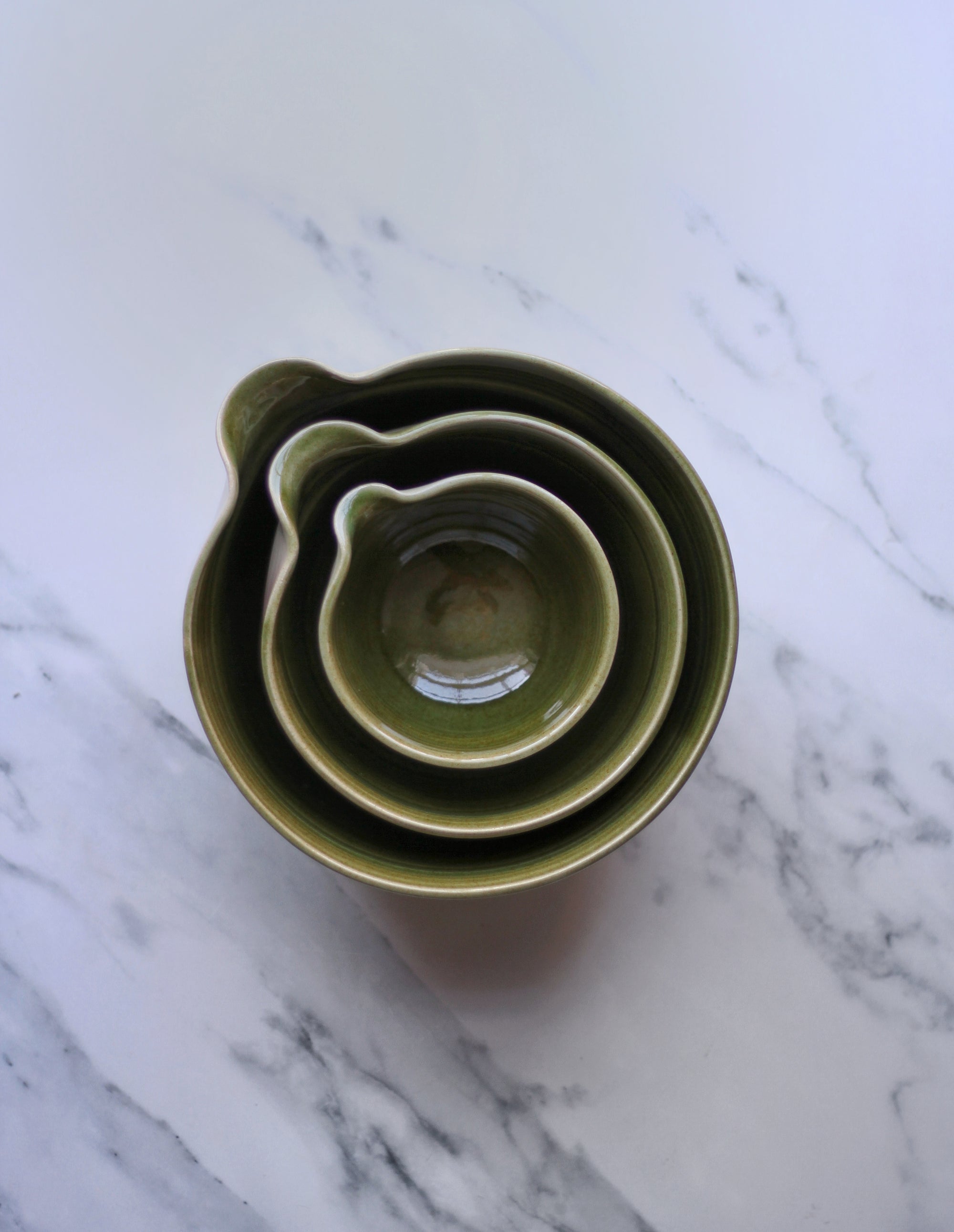 Three green ceramic bowls on a marble surface