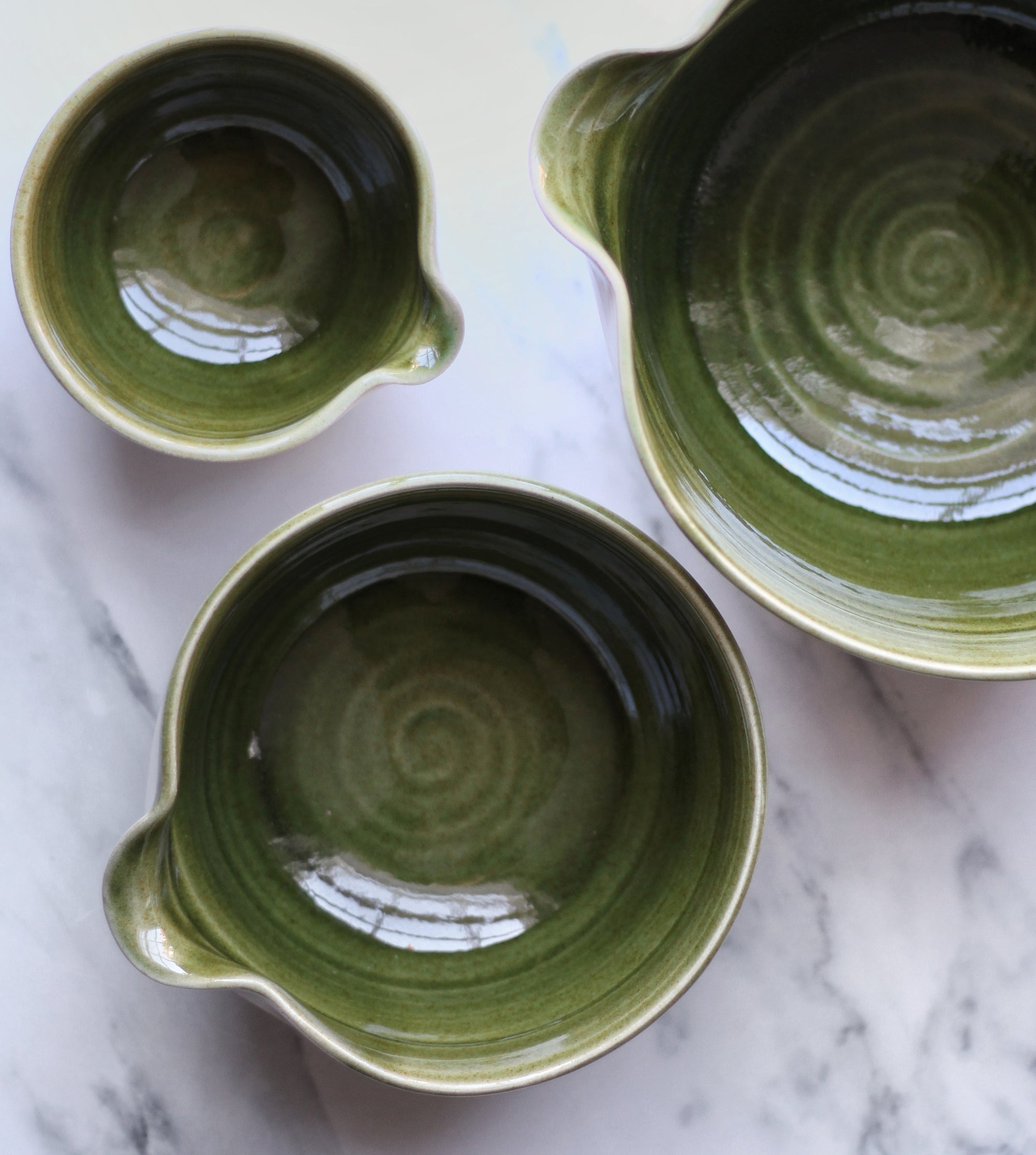 Three green ceramic bowls on a marble surface